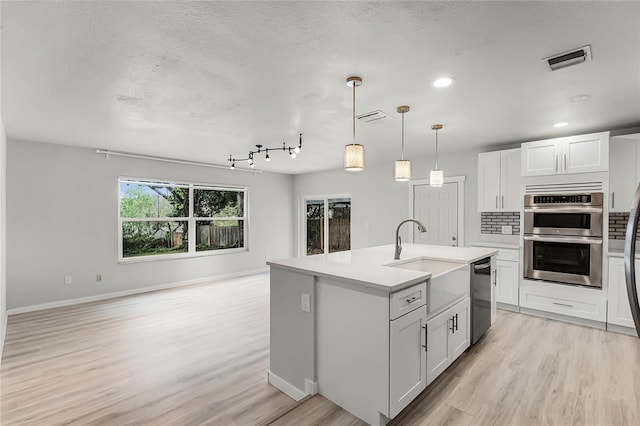 kitchen with a sink, visible vents, open floor plan, appliances with stainless steel finishes, and tasteful backsplash