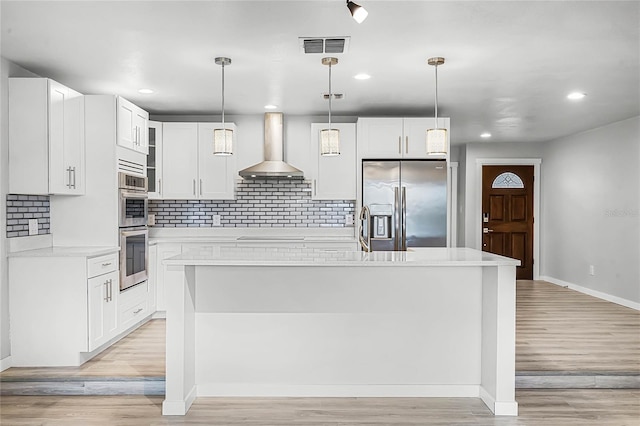 kitchen with light countertops, wall chimney range hood, light wood-style flooring, and appliances with stainless steel finishes