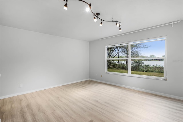 unfurnished room with a water view, light wood finished floors, and baseboards