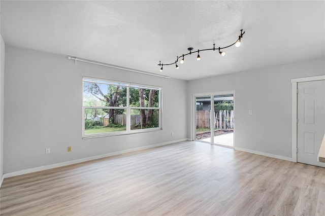 empty room featuring light wood-style floors, baseboards, and a textured ceiling