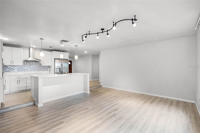 kitchen featuring visible vents, decorative backsplash, wall chimney range hood, light wood-type flooring, and stainless steel fridge