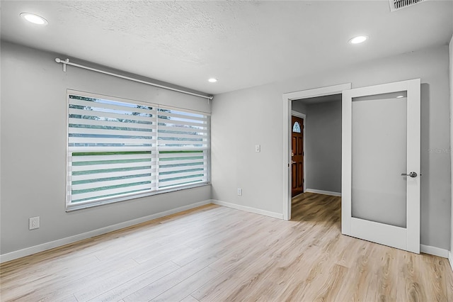 empty room with a textured ceiling, baseboards, wood finished floors, and recessed lighting