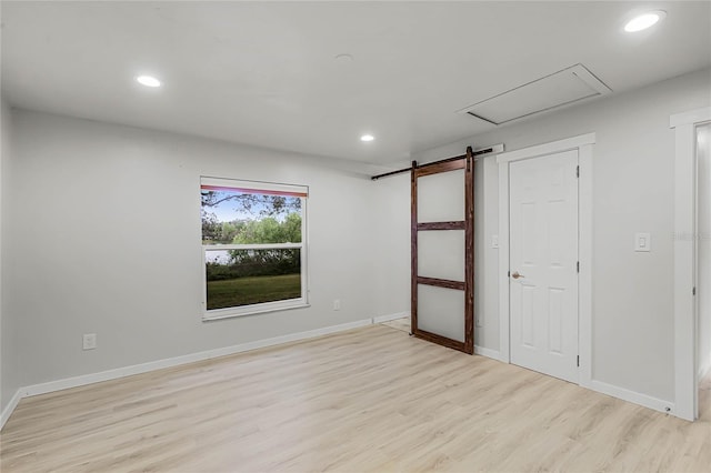 empty room with light wood finished floors, a barn door, and recessed lighting