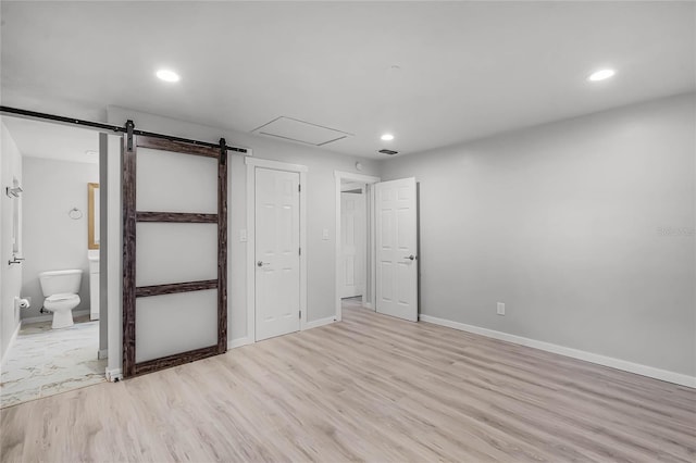 empty room featuring light wood-type flooring, a barn door, baseboards, and recessed lighting