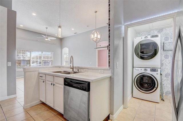 kitchen with stacked washer and clothes dryer, stainless steel dishwasher, white cabinetry, a sink, and light tile patterned flooring