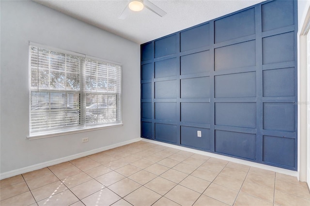 empty room with a ceiling fan, a decorative wall, a textured ceiling, and baseboards