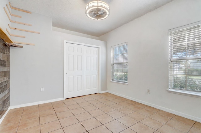 unfurnished bedroom featuring a closet, a textured ceiling, baseboards, and light tile patterned floors