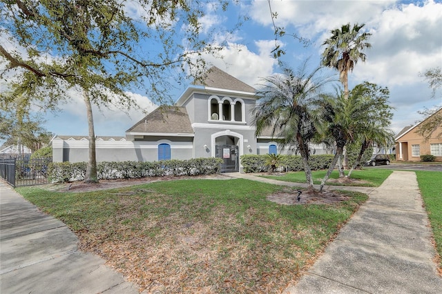 view of front facade with a front yard, roof with shingles, fence, and stucco siding