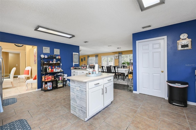 kitchen featuring visible vents, white cabinets, a kitchen island, light countertops, and a textured ceiling