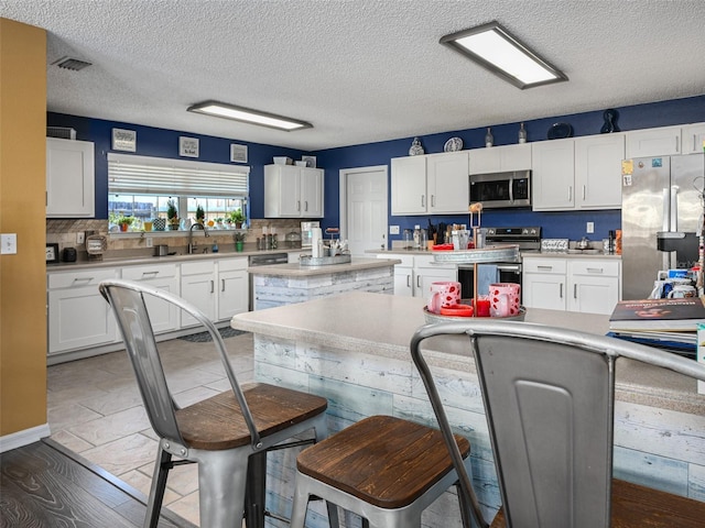 kitchen with light countertops, backsplash, appliances with stainless steel finishes, white cabinetry, and a kitchen island