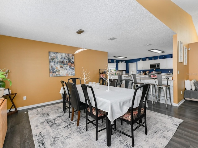 dining area featuring dark wood-style floors, visible vents, a textured ceiling, and baseboards