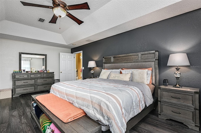 bedroom with dark wood finished floors, a raised ceiling, visible vents, a textured wall, and a textured ceiling