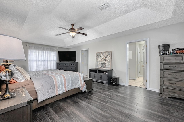 bedroom with a textured ceiling, a tray ceiling, dark wood finished floors, and visible vents