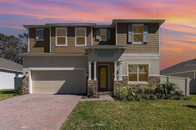 view of front of house with decorative driveway, stucco siding, an attached garage, fence, and stone siding