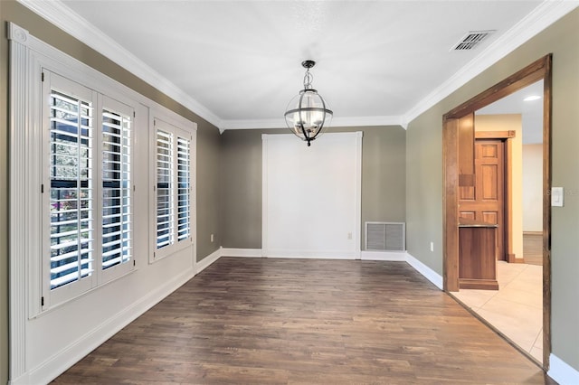 empty room with crown molding, visible vents, a chandelier, and wood finished floors