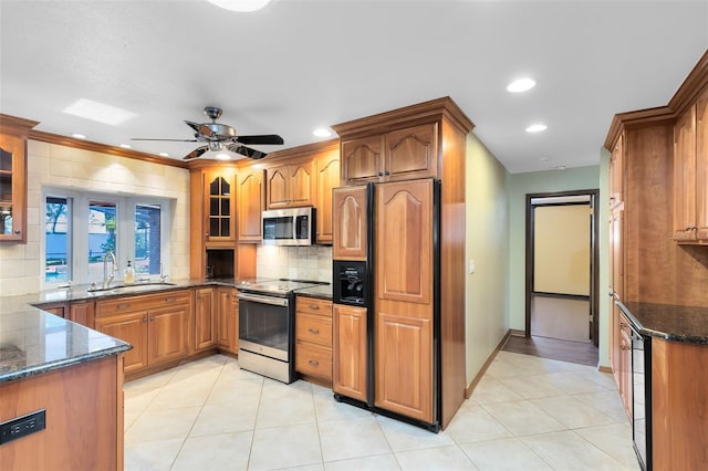 kitchen featuring a sink, appliances with stainless steel finishes, backsplash, dark stone counters, and glass insert cabinets