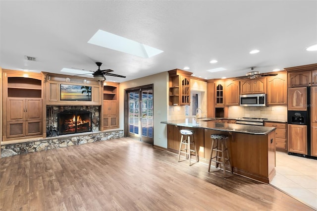 kitchen featuring visible vents, glass insert cabinets, stainless steel appliances, a stone fireplace, and a sink