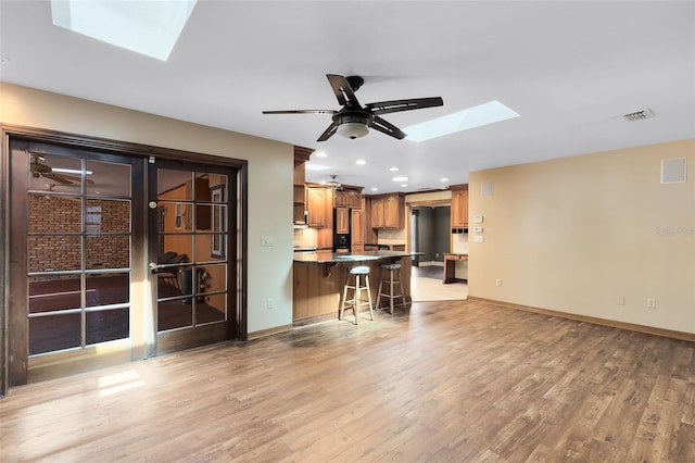 unfurnished living room featuring light wood-type flooring, a skylight, visible vents, and baseboards