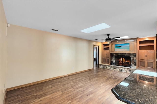 unfurnished living room with baseboards, visible vents, ceiling fan, wood finished floors, and a fireplace