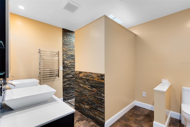 bathroom featuring toilet, visible vents, baseboards, stone finish floor, and radiator heating unit