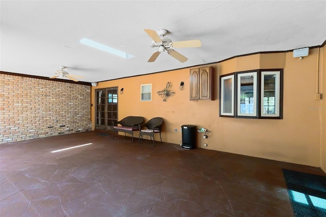 interior space with crown molding, a skylight, ceiling fan, and brick wall