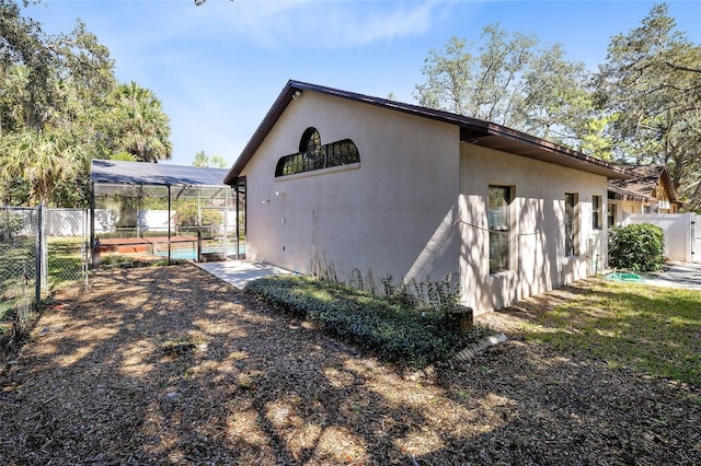 view of side of property with glass enclosure, fence, a gate, and stucco siding