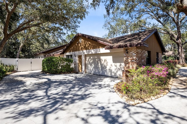 view of side of home with an attached garage, brick siding, fence, driveway, and a gate