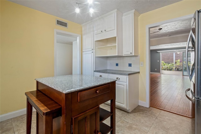 kitchen with visible vents, decorative backsplash, freestanding refrigerator, a textured ceiling, and open shelves