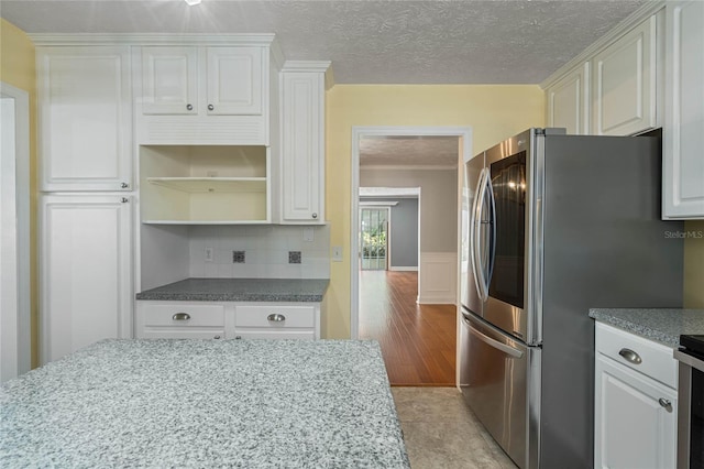 kitchen featuring a wainscoted wall, decorative backsplash, a textured ceiling, white cabinetry, and open shelves