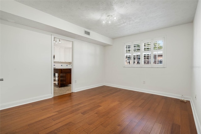 spare room with visible vents, baseboards, a textured ceiling, and hardwood / wood-style floors