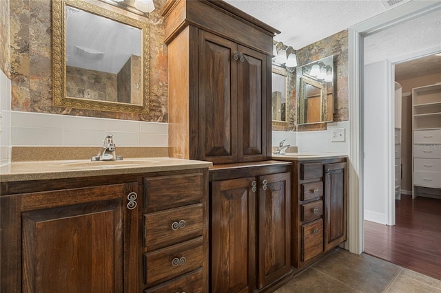 full bath with tile walls, a textured ceiling, two vanities, and a sink