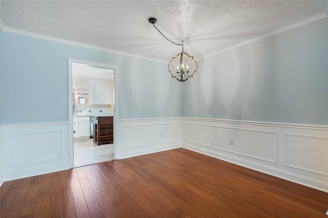 empty room with dark wood finished floors, a textured ceiling, an inviting chandelier, and ornamental molding