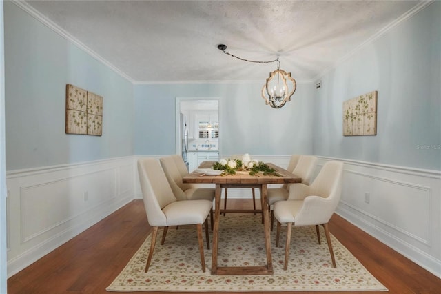 dining area featuring a notable chandelier, dark wood-type flooring, a wainscoted wall, and ornamental molding