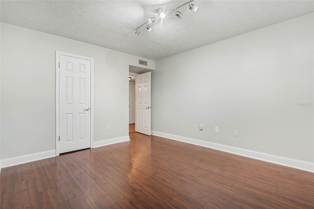 unfurnished bedroom featuring visible vents, track lighting, baseboards, wood finished floors, and a textured ceiling