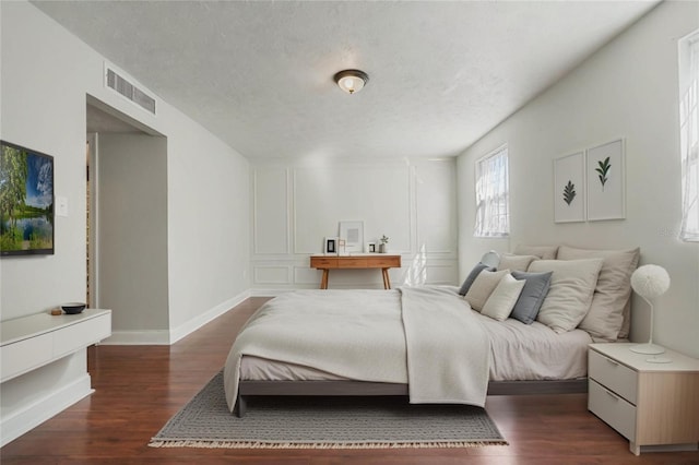 bedroom with baseboards, visible vents, dark wood-style flooring, and a textured ceiling