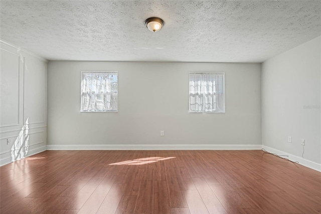 unfurnished room with a textured ceiling, baseboards, and wood-type flooring