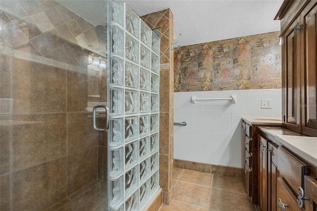 full bath featuring a walk in shower, tile walls, a wainscoted wall, vanity, and a textured ceiling