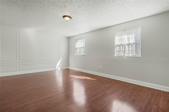 spare room featuring a decorative wall, wood finished floors, baseboards, and a textured ceiling