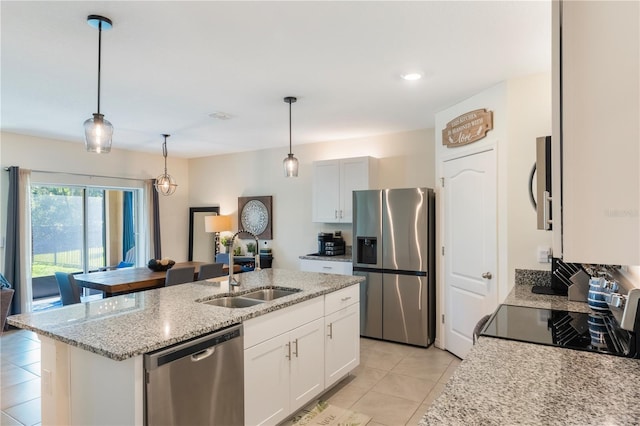 kitchen with light tile patterned floors, stainless steel appliances, a sink, light stone countertops, and an island with sink