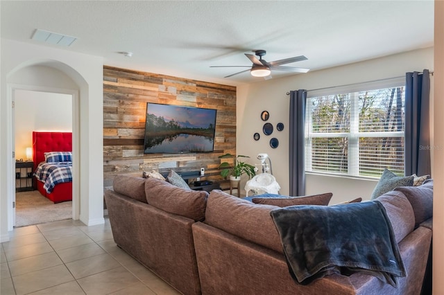 living area featuring light tile patterned floors, visible vents, ceiling fan, an accent wall, and wood walls