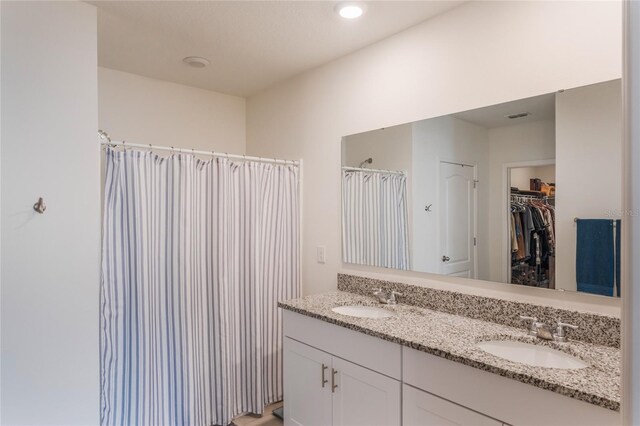 full bath featuring double vanity, a spacious closet, visible vents, and a sink