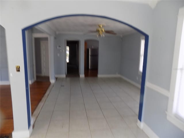 spare room with a ceiling fan, arched walkways, light tile patterned flooring, and baseboards