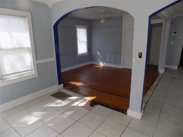 unfurnished room with a wainscoted wall, ceiling fan, arched walkways, and tile patterned floors