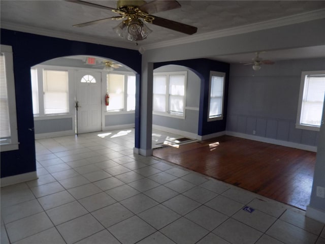 entryway featuring arched walkways, ornamental molding, a ceiling fan, tile patterned flooring, and baseboards