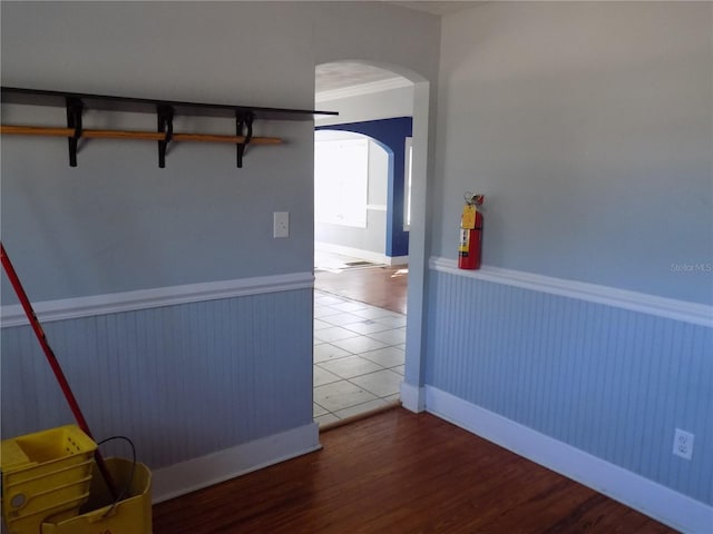 empty room featuring arched walkways, ornamental molding, wood finished floors, and wainscoting