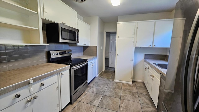 kitchen with open shelves, light countertops, decorative backsplash, appliances with stainless steel finishes, and white cabinetry