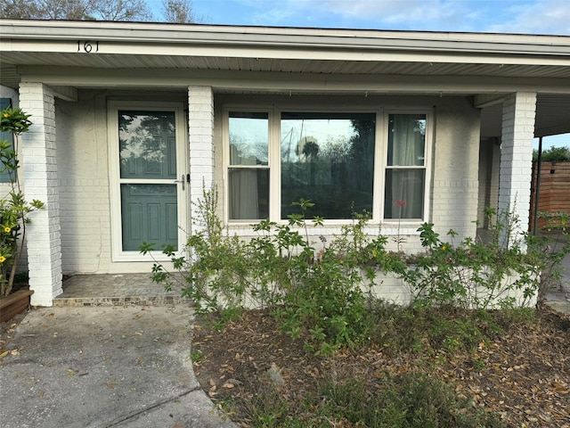 doorway to property featuring covered porch and brick siding