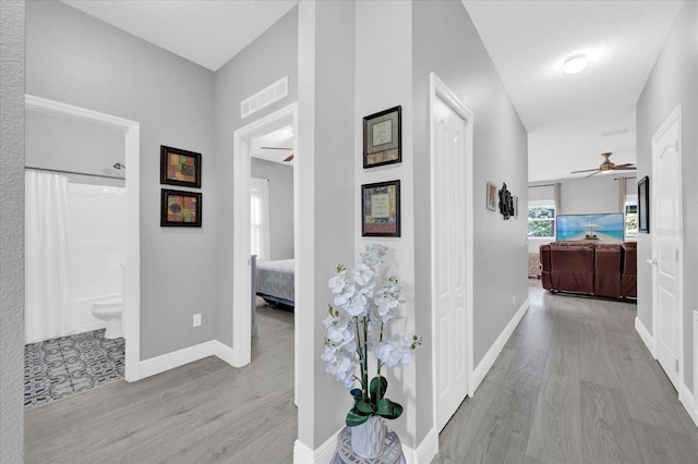 hall featuring wood finished floors, visible vents, and baseboards