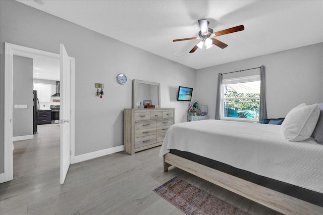 bedroom with light wood-style flooring, a ceiling fan, freestanding refrigerator, and baseboards