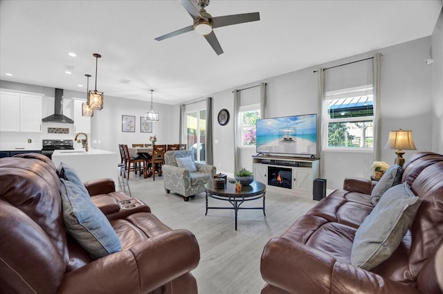 living area with a ceiling fan, a glass covered fireplace, a healthy amount of sunlight, and light wood-style flooring